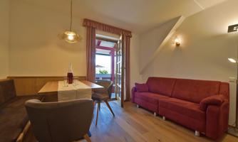 A cozy living space with a red couch and a dining table. Large windows provide a view of a balcony.
