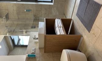 A modern bathroom with a glass shower and a sink on a wooden base. Next to the sink, clean towels are placed on a shelf.