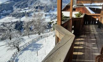 A beautiful balcony with a wooden railing and a view of a snow-covered landscape. The clouds in the sky complement the idyllic winter scenery.