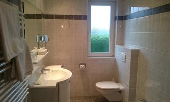 A modern bathroom with bright tiles and a large window. There is a sink, a toilet, and towels on the wall.