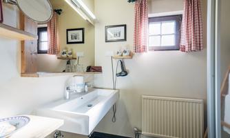 A modern bathroom with a wide sink and mirror. The windows are decorated with checked curtains.