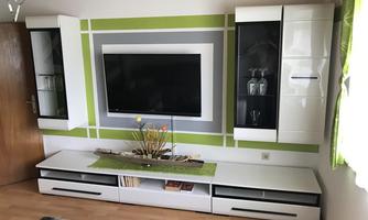 A modernly furnished living room with a television on the wall. The furniture in white and black is complemented by green accents and minimalist decoration.