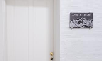 A white door with a golden doorknob. Next to the door is a sign with the inscription "Großvenediger" and a mountain landscape.
