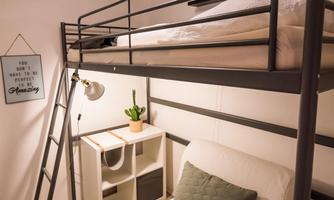 A modern room with a loft bed and a cozy couch. On the wall, there is a small shelf and a plant, surrounded by neutral colors.
