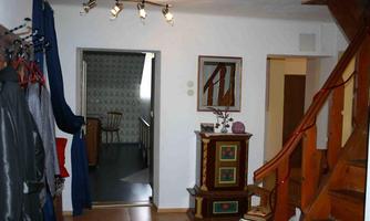 An inviting hallway with a wooden staircase and decorative elements. Clothing hangs on the wall, and there is a view into another room.