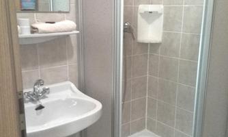 A small bathroom with a shower and a sink. The walls are covered with light tiles.