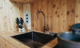 A modern kitchen with wooden paneling, a sink, and a stylish faucet. Next to the sink, kitchen knives are in a holder.