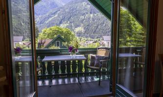 A beautiful balcony with a table and chair that offers a splendid view of the mountains. The surroundings are green and inviting.