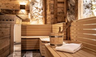 A cozy sauna area made of wood with a wooden bench and bucket. Soft lighting and stone walls create a relaxing atmosphere.