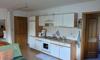A modern kitchen with white cabinets and a countertop. It is simply and functionally furnished, with dishware and appliances.