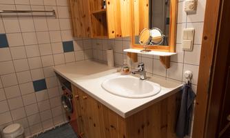 A modern bathroom with wooden shelves and a large mirror. The floor is decorated with white tiles and a blue runner.