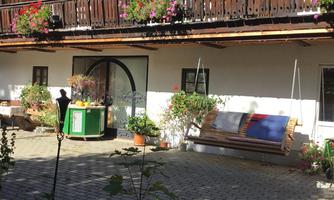 A charming house with balconies adorned with flowers. In the foreground, there is a paved path and some seating options.