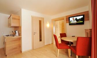 A cozy living space with a round table and red chairs. The modern kitchen and the television on the wall give the room an inviting atmosphere.