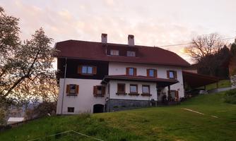 A characteristic house with a red roof, surrounded by green grass and trees. The sky has a gentle gradient at twilight.