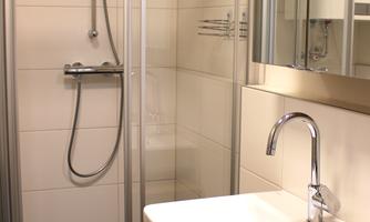 A modern bathroom with a shower and a sink. The walls are brightly tiled and there is a large mirror.