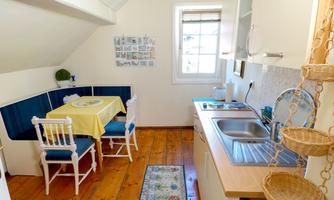 A bright kitchen with a dining area and blue seating benches. The wooden floors and the small rug give it a cozy character.