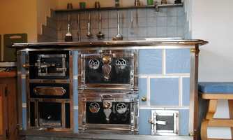 A traditional metal stove with a shiny surface and blue tiles. It is placed in the kitchen area and has various compartments and shelves.