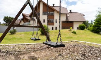 A swing in the playground with a large house in the background. The garden is green and well-maintained.