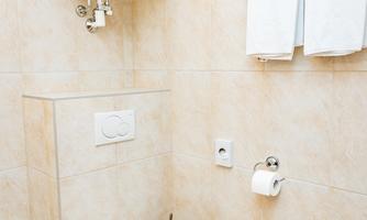 A modern bathroom with a toilet, a towel rack, and a waste bin. The walls are light tiled and the room appears clean and well-maintained.