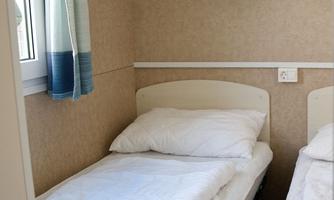 A simple bedroom with two beds and white bedcovers. On the wall are some shelves and a window with curtains.