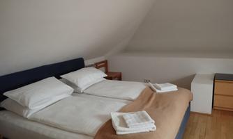 A cozy bedroom with a double bed and fresh bed linens. Next to the bed is a simple nightstand and a desk.