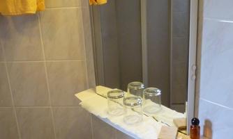 A bathroom with tiles and a mirror is depicted. Three glasses are on a shelf.
