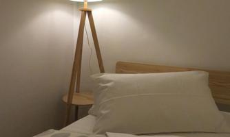 A cozy bedroom with a bed and pillows. A modern floor lamp with a colorful lampshade provides gentle light.