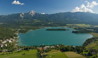 A picturesque lake surrounded by green meadows and mountains in the background. The sky is clear with a few clouds.