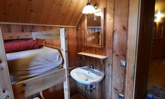 A cozy room with a wooden bunk bed and warm colors. There is a sink and a window that matches the wood paneling.