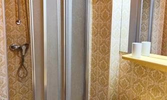 A small bathroom with a shower and a yellow sink. The walls are adorned with a vintage pattern.