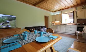 A cozy living space with a dining table and blue dishware. In the background, a modern kitchen and a television can be seen.