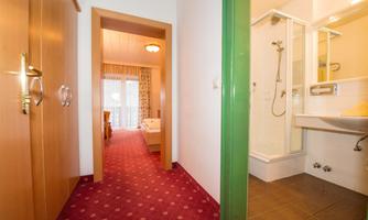 A bright room with a bathroom and a hallway. The floor is red with a carpet, and you can see a shower area.