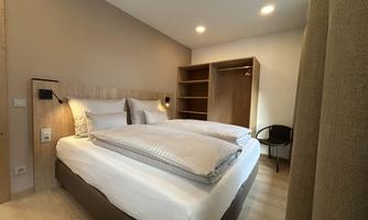 A modern bedroom with a large bed and a cozy decor. There is a wardrobe and soft lighting.