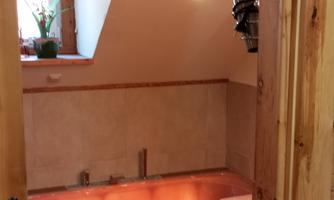 View through a doorway to a rose quartz bathtub with indirect interior lighting under a sloped ceiling, with a small window and tiled wall area.