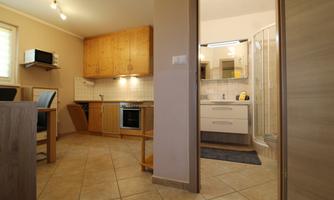 A modern kitchen with wooden furniture and an adjacent bathroom. The room is bright and well-organized.