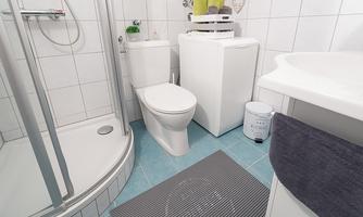 A modern bathroom with a shower, toilet, and washing machine. The floor is tiled in blue and there are towels as well as some decorative items.