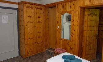 A cozy room with wooden furniture. In the room, there is a wardrobe, a mirror, and a bed with towels.
