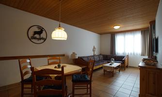 A cozy living room with a dining area and a sofa. The window lets in plenty of daylight, and the wooden ceiling creates a warm atmosphere.