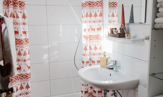 A modern bathroom with a shower and a sink. The walls are tiled in white, and the curtains and the carpet are in vibrant shades of red.