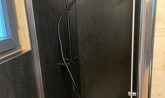 A modern shower with a black showerhead and glass pivoting doors. The walls are made of dark material, which gives an elegant impression.