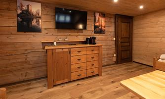 A cozy room with wooden walls and a wooden cabinet. Pictures hang on the wall, and there is a television as well as a coffee machine.