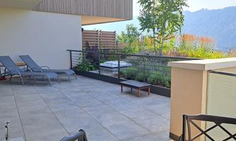 A spacious terrace with two loungers and a small table. In the background, green plants and a beautiful view of the mountains can be seen.