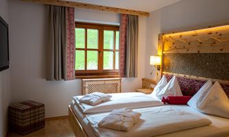 A cozy bedroom with two single beds and modern wooden furniture. A window lets in natural light and creates a bright atmosphere.