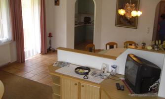 A cozy living area with an open kitchen area. There is a television and bright windows with curtains.