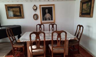 An elegant dining room with a wooden table and six chairs. Several pictures hang on the walls and there is a rug on the floor.