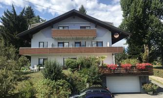 A modern house with a large balcony and flower boxes. Surrounded by trees and green land.