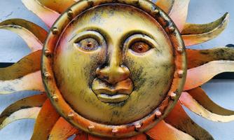 A sun-shaped wall decoration with a face in gold and orange tones. The rays are artistically designed, giving the sun a warm, inviting look.