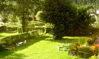 A beautiful garden with green grass and trees. Some chairs are ready to enjoy nature.