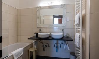 A modern bathroom with two sinks, a large mirror, and a bathtub. The walls are painted in neutral colors, and towels are neatly hung on a towel rack.