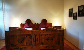 A cozy bedroom with a wooden double bed and upholstered headboards. Decorative pictures hang on the walls, and there is soft lighting.